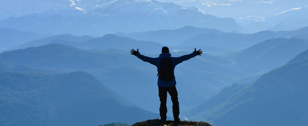 Man standing on peak with arms spread wide.